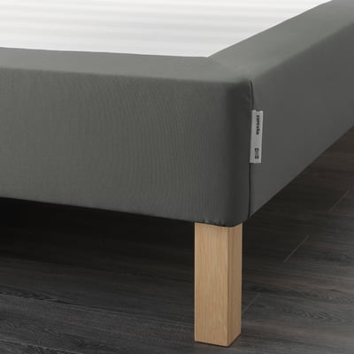 A modern bed frame with a grey fabric cover and wooden legs, providing extra support and height for a comfortable sleep.
