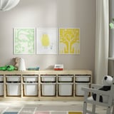Three colorful framed pictures above wooden shelf with toy-filled bins.