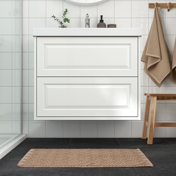 Modern bathroom with white cabinet, beige FJÄLLKATTFOT mat, and wood stool. Mat is plush, fits under cabinet, adds warmth.