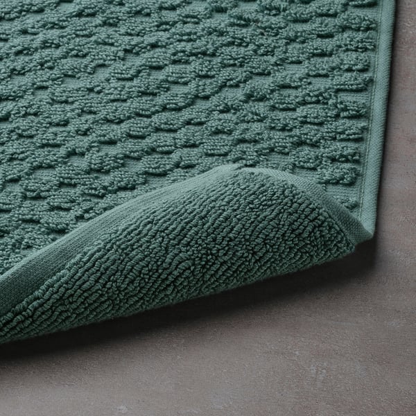 Green, textured bath mat close-up, showcasing its soft terry and high absorption. Fitted corner reveals plush design.