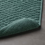 Green, textured bath mat close-up, showcasing its soft terry and high absorption. Fitted corner reveals plush design.