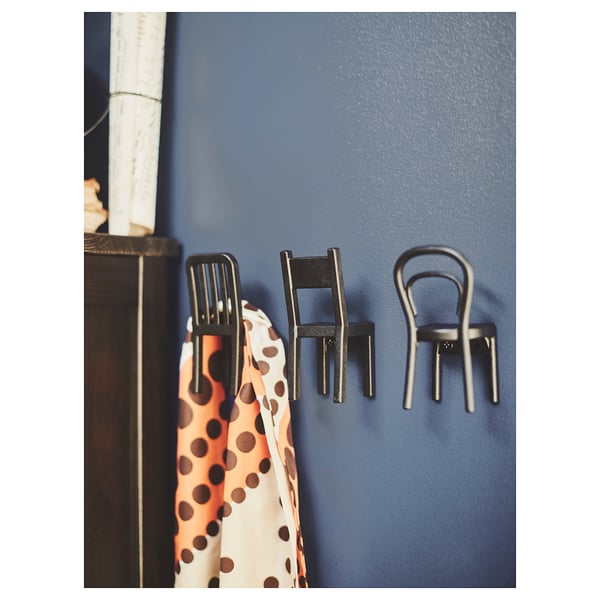 Three decorative chair-shaped black hooks on a blue wall. One holds a scarf. Modern and playful design in reinforced plastic.