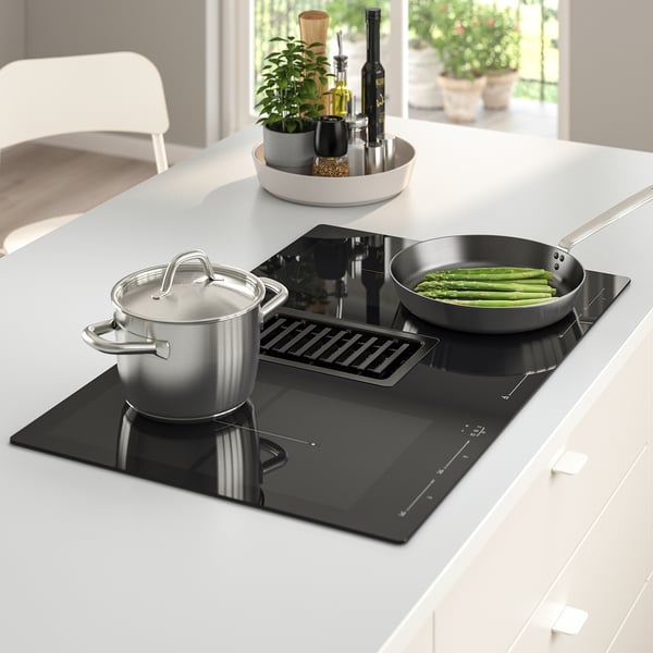 Modern kitchen with black FÖRDELAKTIG induction hob, stainless cookware, asparagus, bottles, plants.