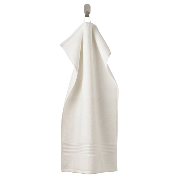 The FREDRIKSJÖN towel is white, soft, thick, and made of 100% cotton. It hangs neatly on a hook, featuring a subtle woven border.