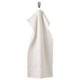 The FREDRIKSJÖN towel is white, soft, thick, and made of 100% cotton. It hangs neatly on a hook, featuring a subtle woven border.
