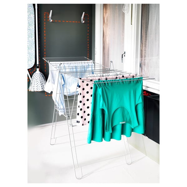 A white FROST drying rack with colorful clothes drying indoors. Its foldable and made of powder-coated steel.