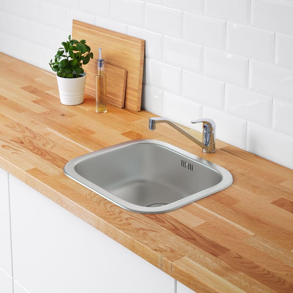 Wood countertop with stainless steel sink and faucet, white tiled wall.