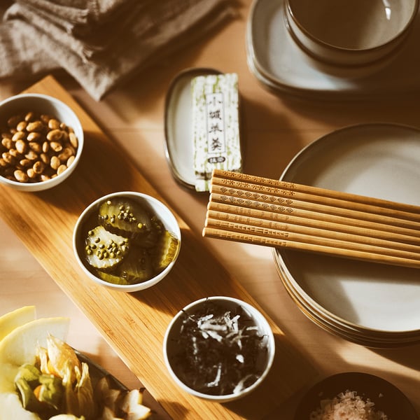 Wooden serving board with bowls of snacks, chopsticks, and small dishes on a dining table.
