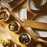 Wooden serving board with bowls of snacks, chopsticks, and small dishes on a dining table.