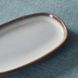 Brown-rimmed elliptical dish with smooth glaze on blue cloth.