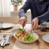Person eating salad with fork and knife. Plate, glass, and napkin on table.