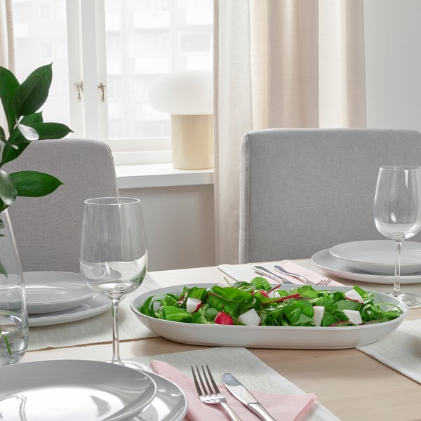White dinnerware set with salad, cutlery, glasses, napkins near window.