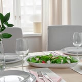 White dinnerware set with salad, cutlery, glasses, napkins near window.