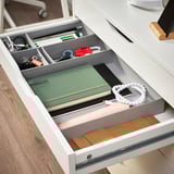 Organized desk drawer with GRÅSIDAN boxes: notebooks, scissors, keys, and cords sorted in small, medium, and large boxes.