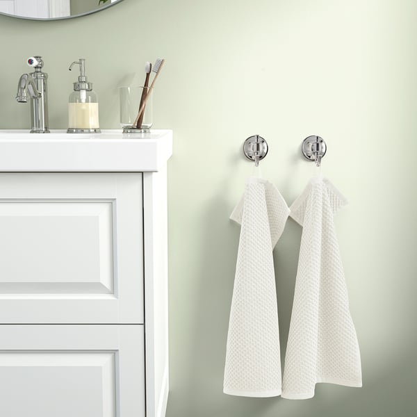A bathroom with a white vanity, soft beige GULVIAL towels, and chrome hooks. Light color scheme.