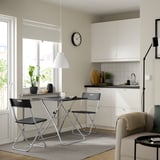 Modern kitchen/dining area with GUNDE table, chairs, and cream armchair. Bright with white cabinets and large window, grey rug, pendant lamp.