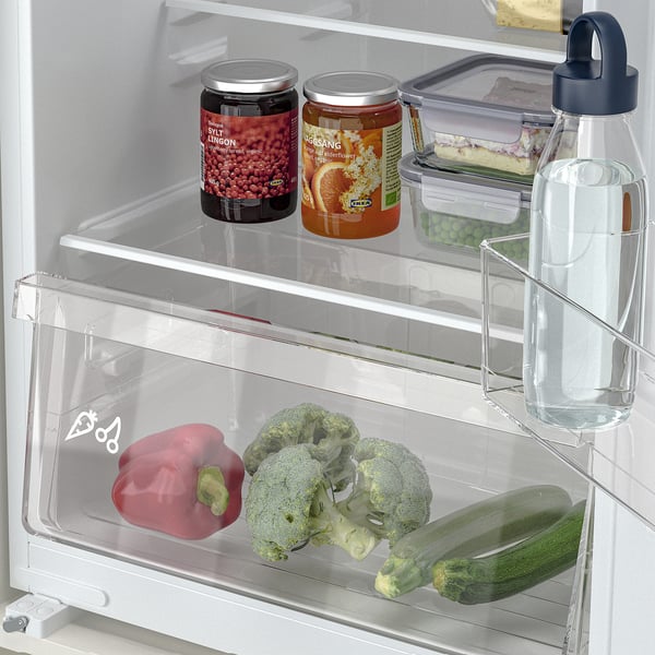 A fridge with adjustable shelves holding jars, veggies, and a water bottle.