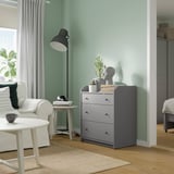 Modern bedroom with gray HAUGA chest, white curtains, green wall, and wooden floor.