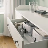Open white kitchen drawer showing organized white and gray storage boxes containingsalt and pepper shakers, napkins, and cutlery.