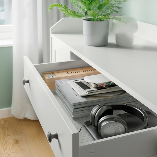 Open white drawer with headphones, books, and stationery. Plant on top.
