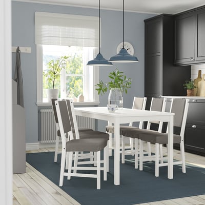 Modern white HAUGA dining set with 6 gray upholstered chairs in cozy kitchen, surrounded by black cabinets and wood floors.