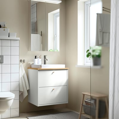 Minimalist bathroom with HAVBÄCK sink, bamboo counter, wall cabinet, stool with magazines, plant, and large mirror.
