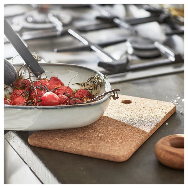 White bowl of tomatoes on black stove, beige cork stand beside.