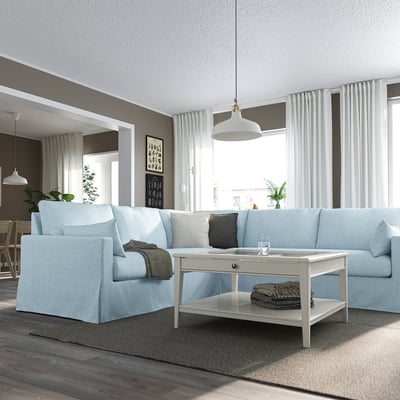 Large light blue sectional sofa with white coffee table, arched lamp, grey blankets, and white curtains in modern living space.