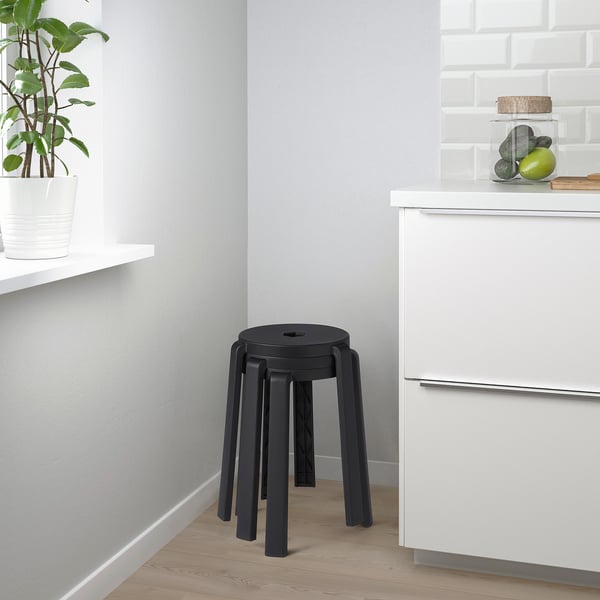 Small modern kitchen with black stackable stool against white cabinet.