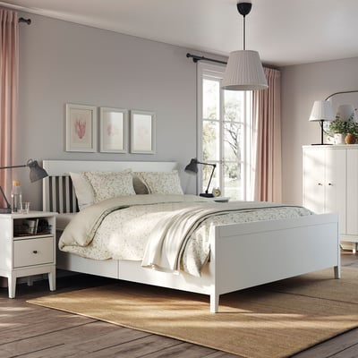 Modern bedroom with IDANÄS white storage bed, light curtains, floral bedding, sleek side tables, and soft ambient lighting.