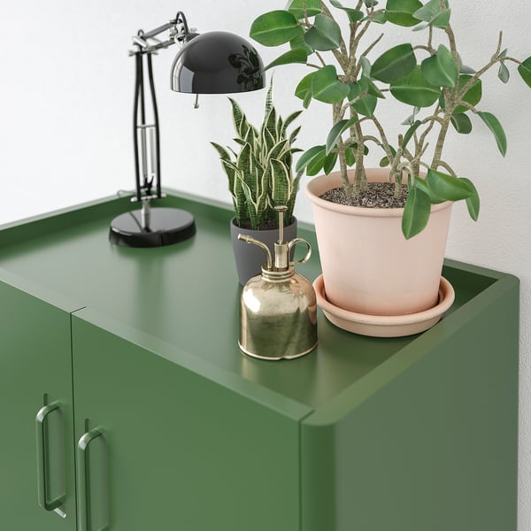 Green cabinet with lamp, two plants, and golden bell on top.