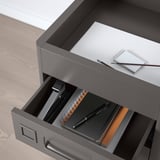Gray metal drawer unit with pen, notebook, and binder inside; designed for office use with integrated dampers for silent closure.