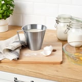 Kitchen prep: steel measuring cup, shells, cloth, plant, jars.