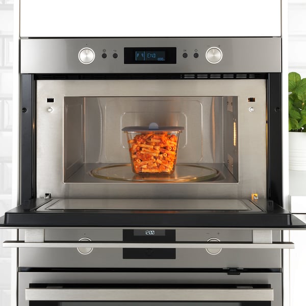 Stainless steel microwave with glass container, showing vacuum lid for food freshness.