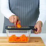Person grates carrot directly into glass container using IKEA 365+ grater on wooden board.