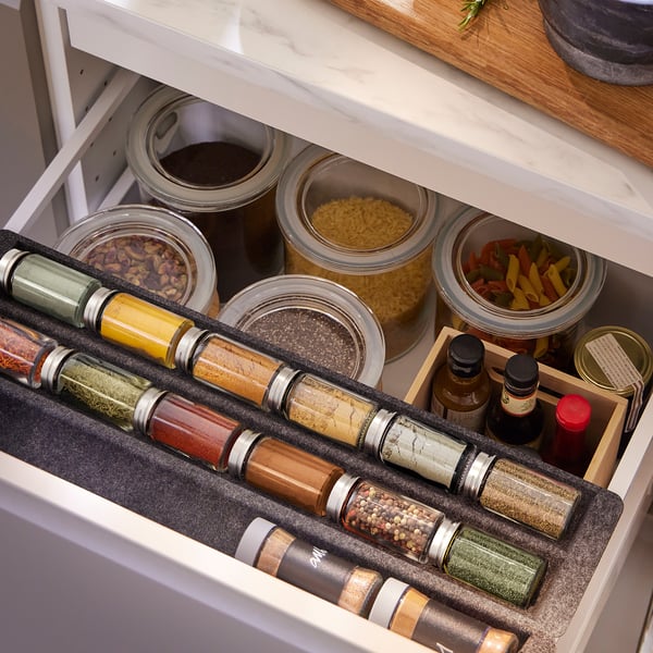Kitchen drawer with spice jars, pasta, and sauces; transparent jars for easy identification.