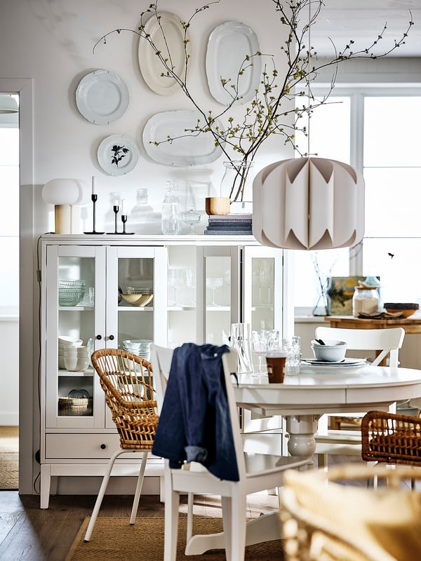 Bright dining space with white INGATORP extendable table, wicker chairs, glass cabinet, and wall-mounted plates. Modern, clean design.