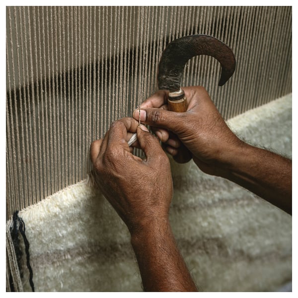 Hands crafting JULGRANSGRÄS rug, weaving wool into striped, sandy texture.