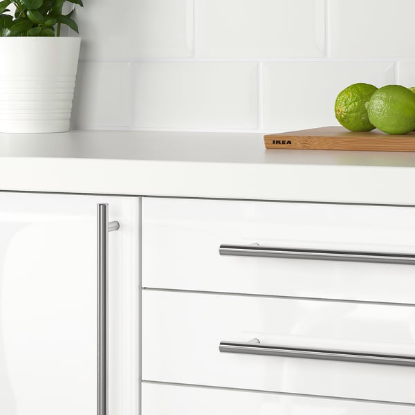 Modern kitchen with white cabinets and metallic handles. A white countertop holds a plant and limes.