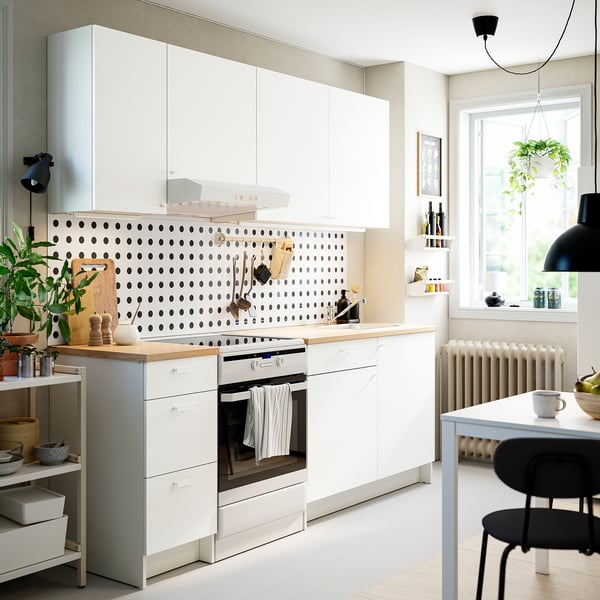 Modern white kitchen with black polka-dot backsplash, stainless appliances, hanging plants, and black chairs.