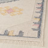 Handwoven cream rug with colorful geometric designs; fringed edges, natural wool texture.