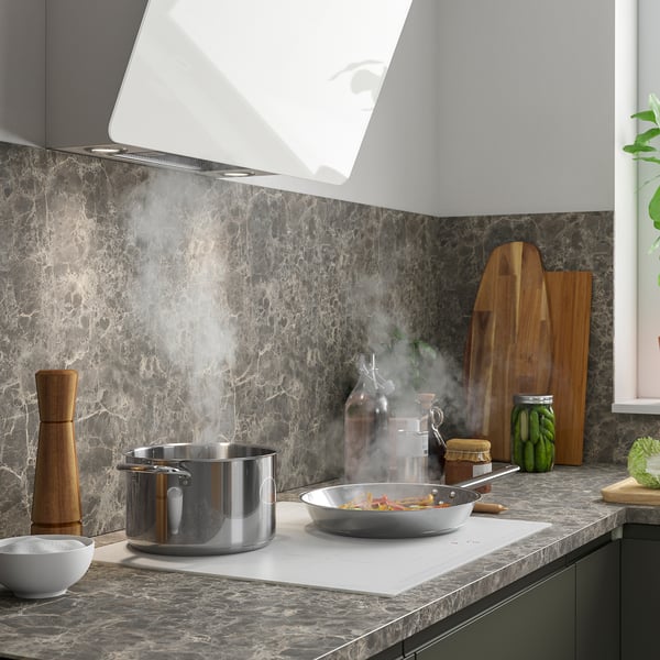 Modern kitchen with marble backsplash, active cooking with veggies, and organized condiments.