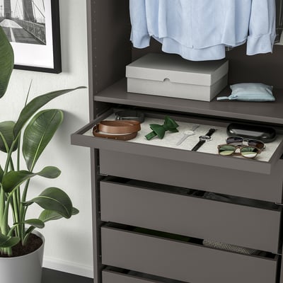 Gray drawer with accessories tray on felt mat. Plant and shelf above with clothes and box.
