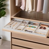 Organized drawer with compartments for jewelry and accessories in a well-lit closet.