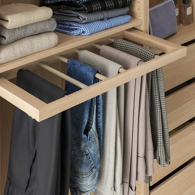 A wooden trousers hanger pulled out for easy access, holding multiple pairs of neatly organized pants in a pax wardrobe.