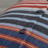 Close-up of striped cushion cover with fabric-covered button. Dark blue, red, and white stripes on textured fabric.