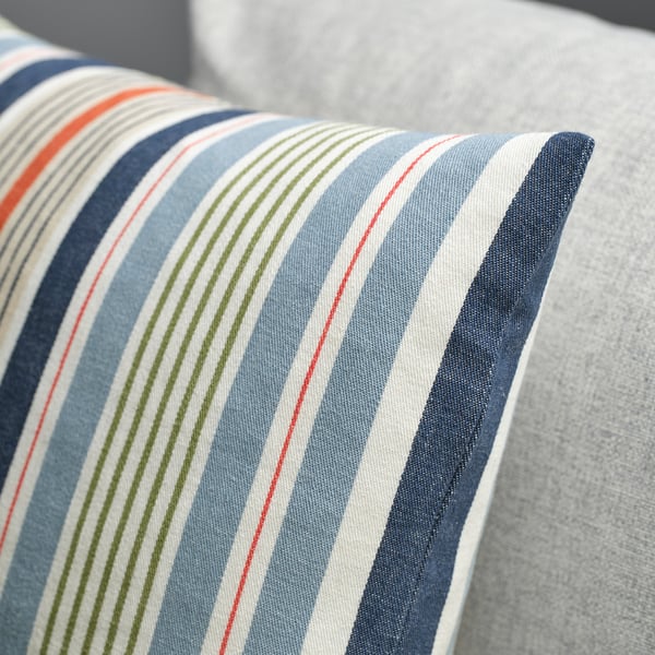 Striped cushion cover on a sofa, multicolored stripes on blue-gray background, neatly sewn with a zipper closure.
