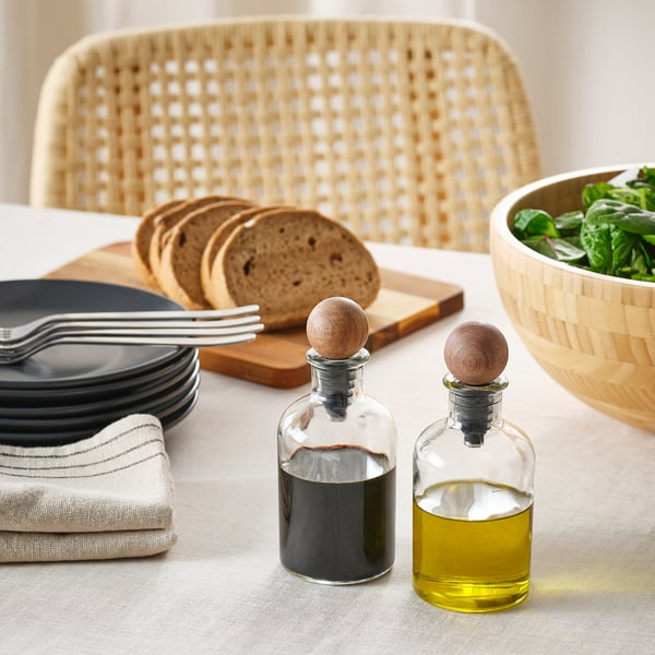 Dining table with glass bottles of oil and vinegar, bread, plates, and forks; two wooden-stopped bottles.