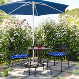 Black chairs with blue cushions, umbrella, red drinks in garden with white flowers.