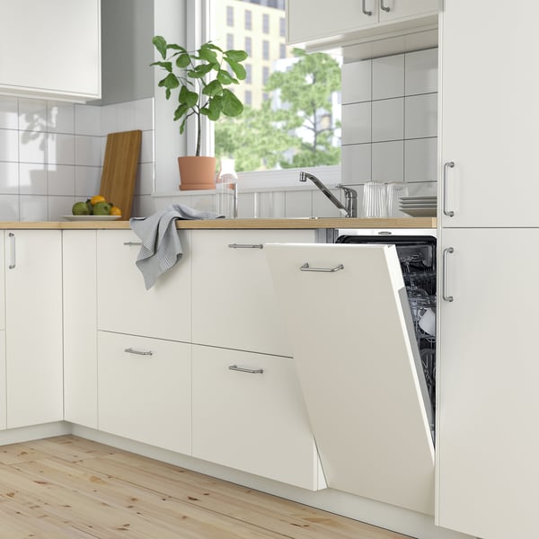 Modern white kitchen with integrated dishwasher open, next to potted plant and window.